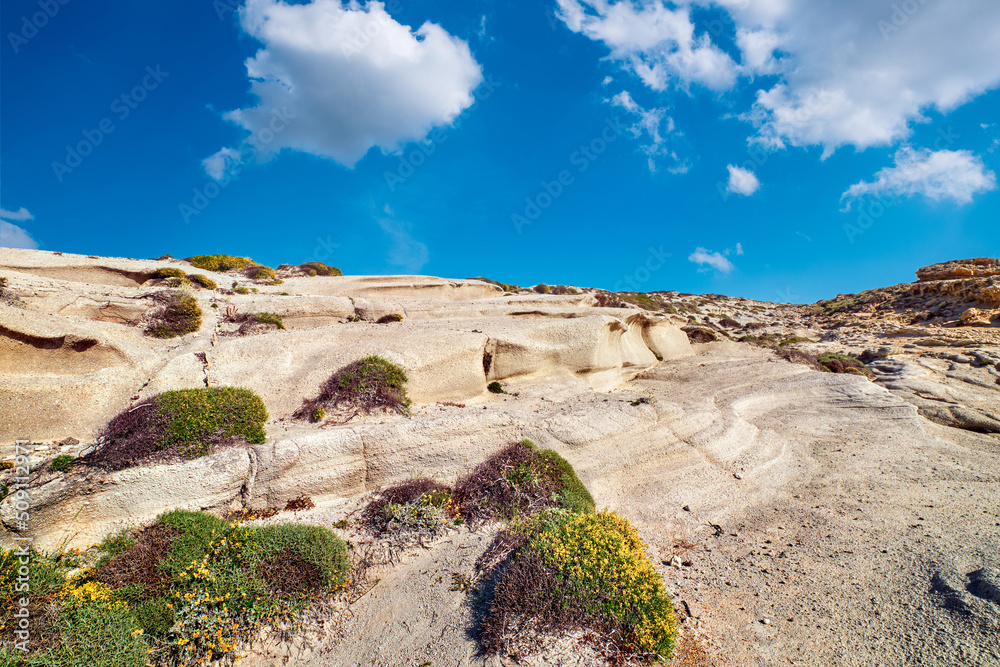 Summer landscape of rocks on Sarakiniko beach, Aegean sea, Milos island , Greece. No people, empty cliffs, sunshine, blue sky and clouds, some grass