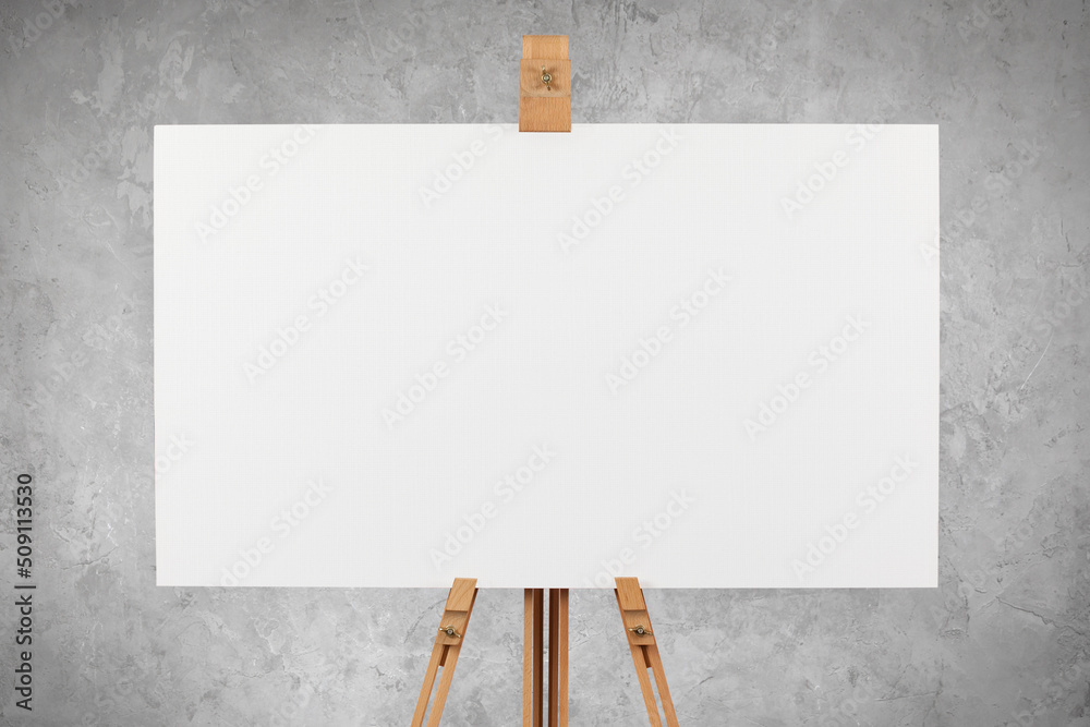 A blank artist's canvas on an easel against a concrete wall background.
 - obrazy, fototapety, plakaty 