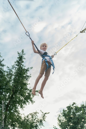 Boy rides trampoline in an amusement park and jumps high into sky. Child has fun in the theme park.