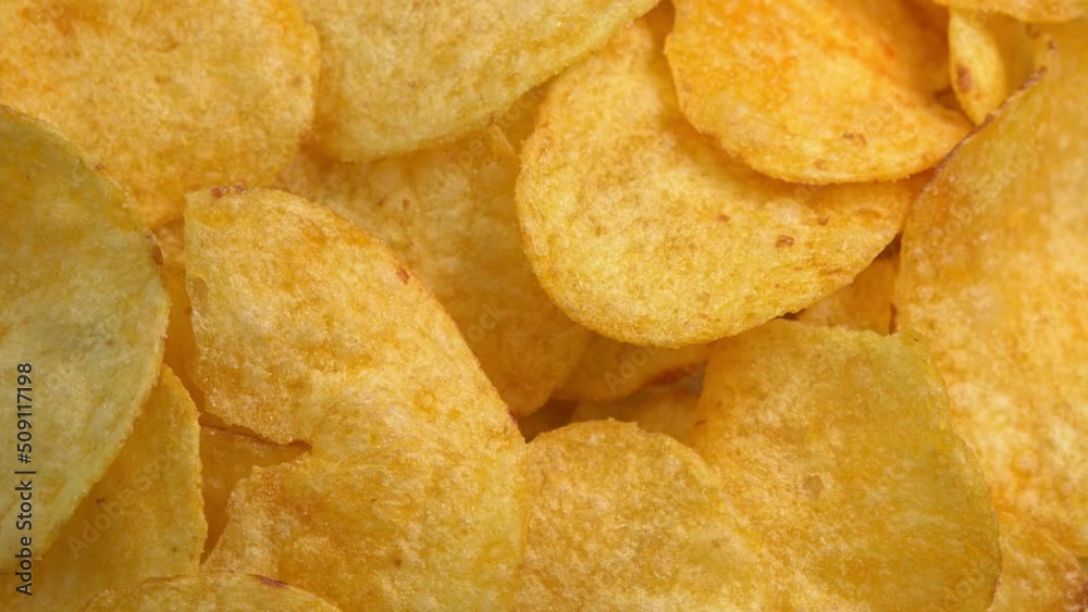 Crispy potato chips rotating in macro. Golden fried potatoes close up. Potato snack for unhealthy fast food. High quality 4k footage Crispy potato chips rotating in macro. Golden fried potatoes close up. Potato snack for unhealthy fast food. High quality 4k footage