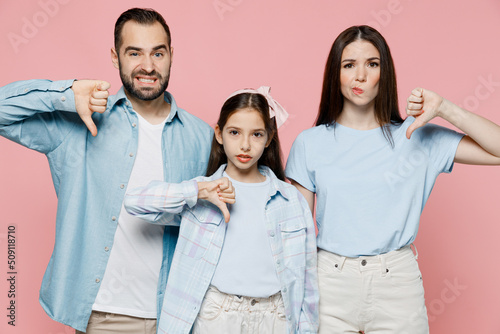 Young happy parents mom dad with child kid daughter teen girl in blue clothes showing thumb down dislike gesture isolated on plain pastel light pink background Family day parenthood childhood concept