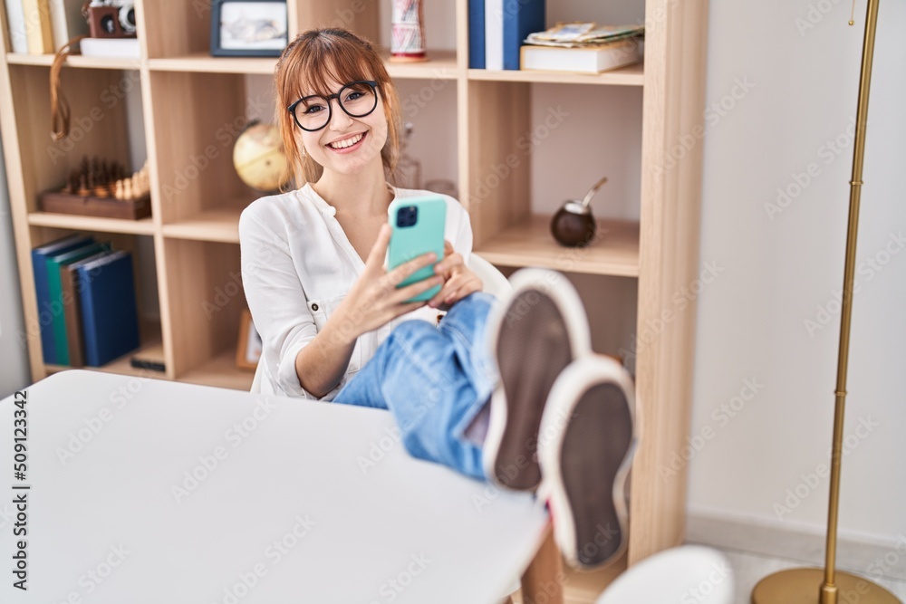 Young woman using smartphone sitting on table at home Young woman using smartphone sitting on table at home