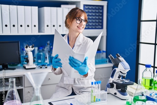 Young woman scientist smiling confident reading report at laboratory