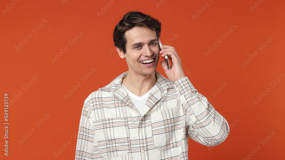Happy calm smiling vivid young brunet man 20s years old wears white shirt hold use talk on mobile cell phone conducting pleasant conversation isolated on plain orange wall background studio portrait Happy calm smiling vivid young brunet man 20s years old wears white shirt hold use talk on mobile cell phone conducting pleasant conversation isolated on plain orange wall background studio portrait