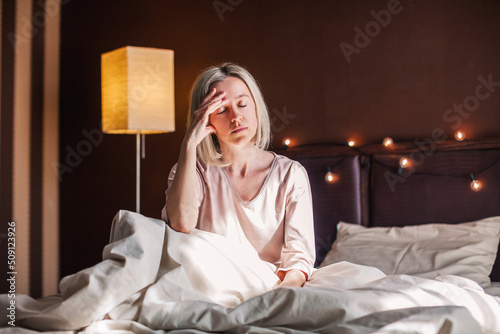 Unhappy sad middle aged woman sitting on bed at home photo