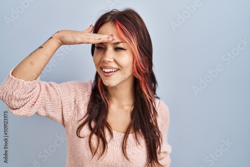 Young caucasian woman wearing pink sweater over isolated background very happy and smiling looking far away with hand over head. searching concept.