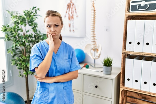 Young caucasian woman working at pain recovery clinic thinking looking tired and bored with depression problems with crossed arms.