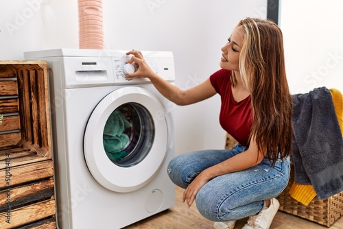 Young caucasian girl smiling happy cleaning clothes using whasing machine at home.