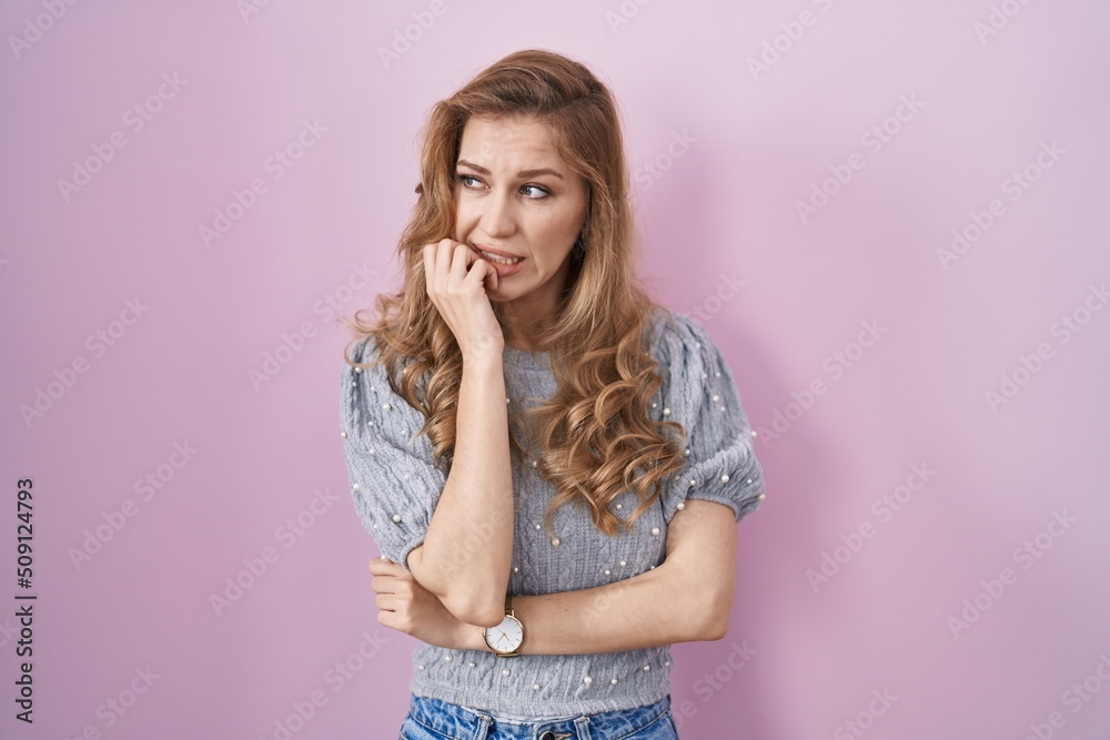 Beautiful blonde woman standing over pink background looking stressed and nervous with hands on mouth biting nails. anxiety problem. Beautiful blonde woman standing over pink background looking stressed and nervous with hands on mouth biting nails. anxiety problem.