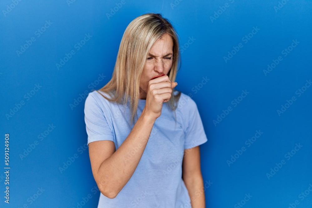 Beautiful blonde woman wearing casual t shirt over blue background feeling unwell and coughing as symptom for cold or bronchitis. health care concept. Beautiful blonde woman wearing casual t shirt over blue background feeling unwell and coughing as symptom for cold or bronchitis. health care concept.