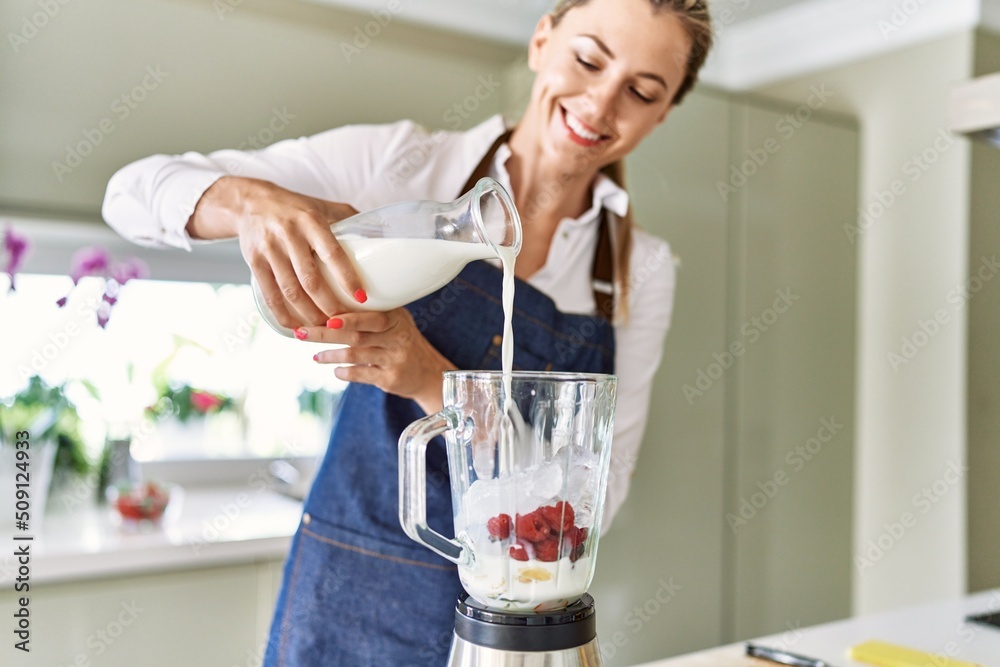 Woman in orange dress pouring fresh milk into electric blender Stock Photo  by Pressmaster