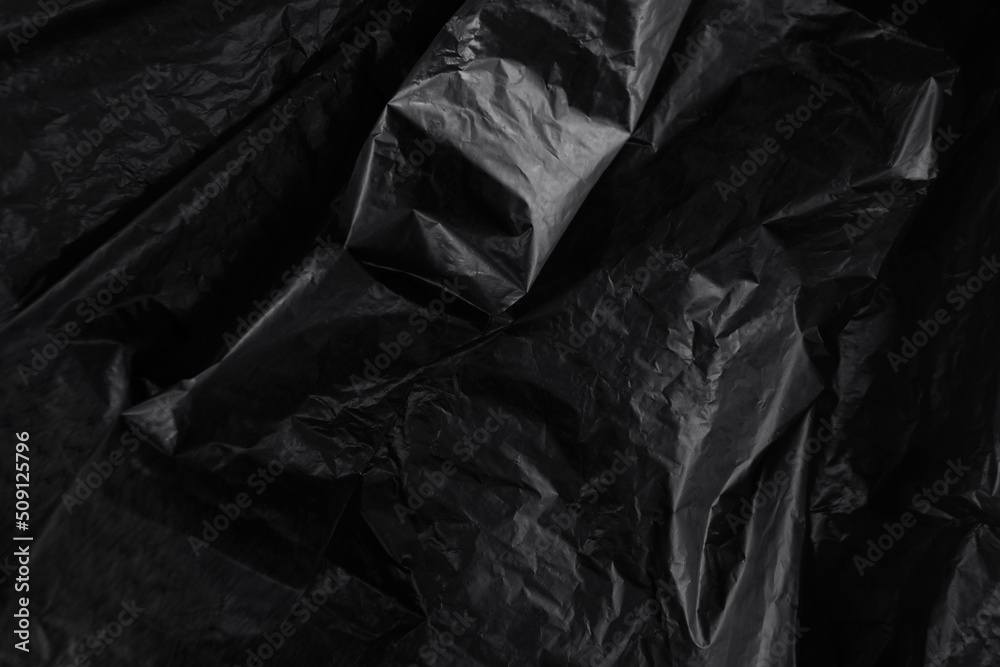 Closeup crumpled single use or non recyclable black color plastic trash bag made from polyethylene texture background