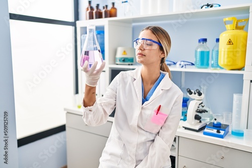 Young hispanic woman scientist measuring liquid at laboratory