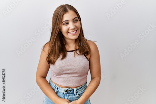 Young brunette woman standing over isolated background looking away to side with smile on face, natural expression. laughing confident.