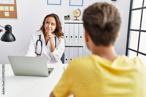 Young doctor woman with patient at the clinic serious face thinking about question with hand on chin  thoughtful about confusing idea