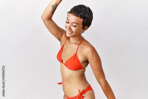 Young hispanic woman with short hair wearing bikini dancing happy and cheerful, smiling moving casual and confident listening to music