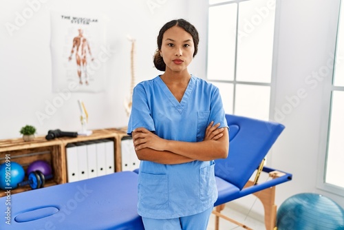 Beautiful hispanic physiotherapist woman at pain recovery clinic skeptic and nervous, disapproving expression on face with crossed arms. negative person.