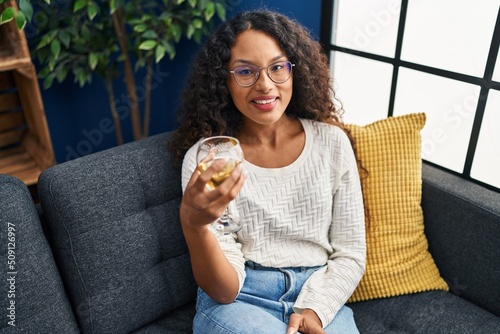 Young latin woman drinking champagne sitting on sofa at home