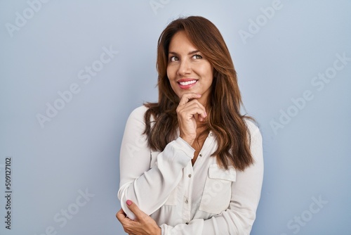 Hispanic woman standing over isolated background with hand on chin thinking about question, pensive expression. smiling and thoughtful face. doubt concept.