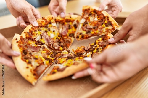 Hands of people taking portion of italian pizza on the table at home.