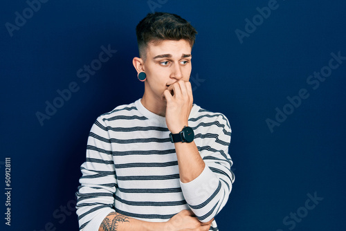 Young caucasian boy with ears dilation wearing casual striped shirt looking stressed and nervous with hands on mouth biting nails. anxiety problem.