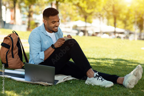Bilde på lerret Happy black male student studying remotely with laptop and writing down informat