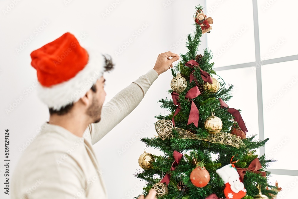 Young hispanic man smiling happy decorating christmas tree at home. Young hispanic man smiling happy decorating christmas tree at home.