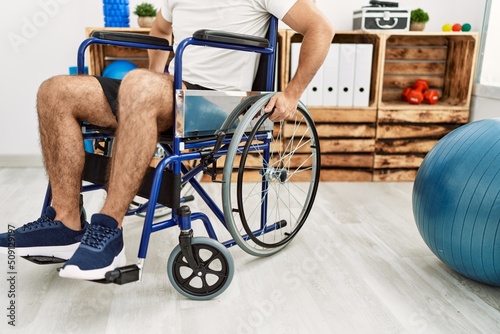 Young hispanic man sitting on wheelchair at clinic