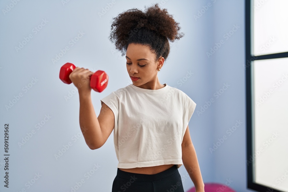 Young african american woman training using dumbbell at sport center