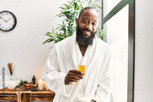 Young african american man smiling confident drinking champagne at beauty center