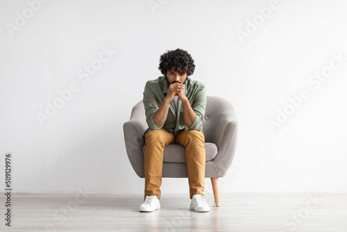 Fototapeta Depressed indian guy sitting in armchair over white