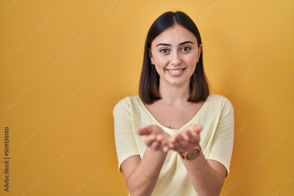 Hispanic girl wearing casual t shirt over yellow background smiling with hands palms together receiving or giving gesture. hold and protection Hispanic girl wearing casual t shirt over yellow background smiling with hands palms together receiving or giving gesture. hold and protection