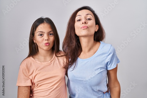 Young mother and daughter standing over white background looking at the camera blowing a kiss on air being lovely and sexy. love expression.