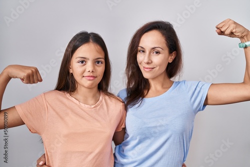 Young mother and daughter standing over white background strong person showing arm muscle  confident and proud of power