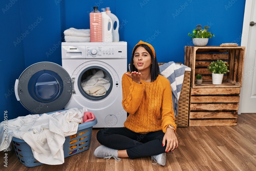 Young hispanic woman doing laundry looking at the camera blowing a kiss with hand on air being lovely and sexy. love expression. Young hispanic woman doing laundry looking at the camera blowing a kiss with hand on air being lovely and sexy. love expression.