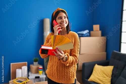 Young latin woman talking on the smartphone choosing color paint wall at new home