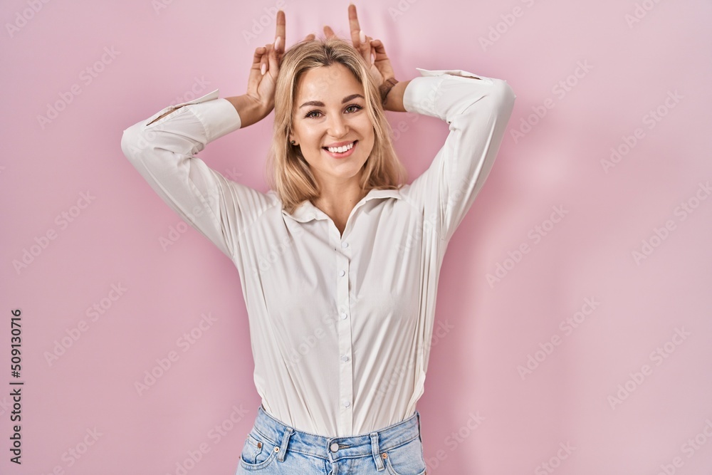 Young caucasian woman wearing casual white shirt over pink background posing funny and crazy with fingers on head as bunny ears, smiling cheerful Young caucasian woman wearing casual white shirt over pink background posing funny and crazy with fingers on head as bunny ears, smiling cheerful