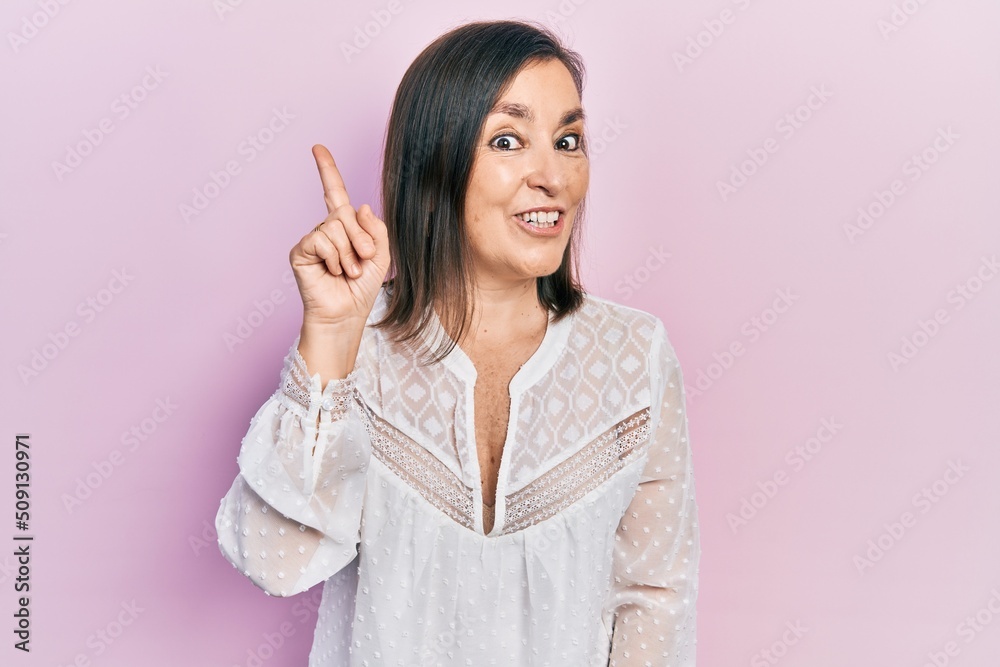 Fototapeta premium Middle age hispanic woman wearing casual clothes showing and pointing up with finger number one while smiling confident and happy.