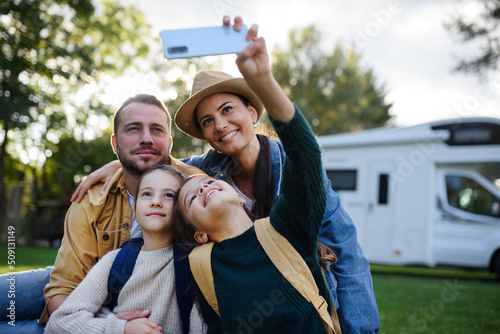 Happy young family with two children taking selfie with caravan at background outdoors. photo