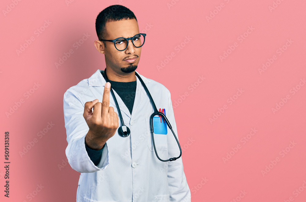 Young african american man wearing doctor uniform and stethoscope showing middle finger, impolite and rude fuck off expression Young african american man wearing doctor uniform and stethoscope showing middle finger, impolite and rude fuck off expression