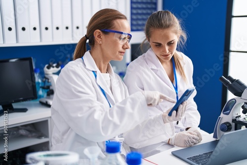 Two women scientists using smartphone working at laboratory