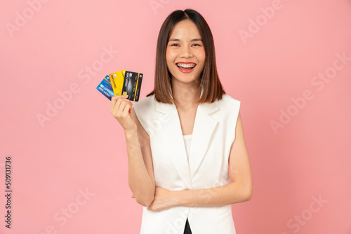 Cheerful beautiful Asian woman holding mockup credit card on pink background.