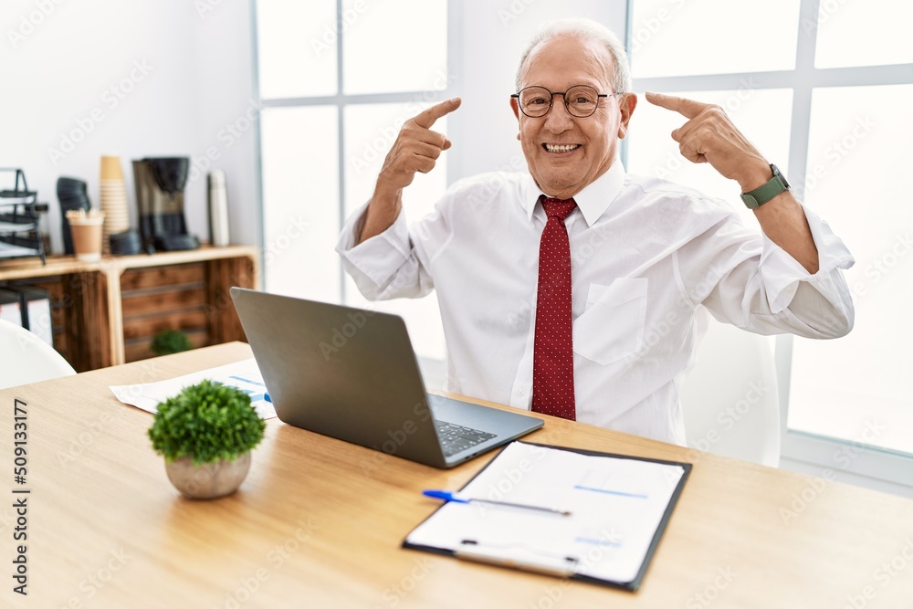 Senior man working at the office using computer laptop smiling pointing to head with both hands finger, great idea or thought, good memory Senior man working at the office using computer laptop smiling pointing to head with both hands finger, great idea or thought, good memory