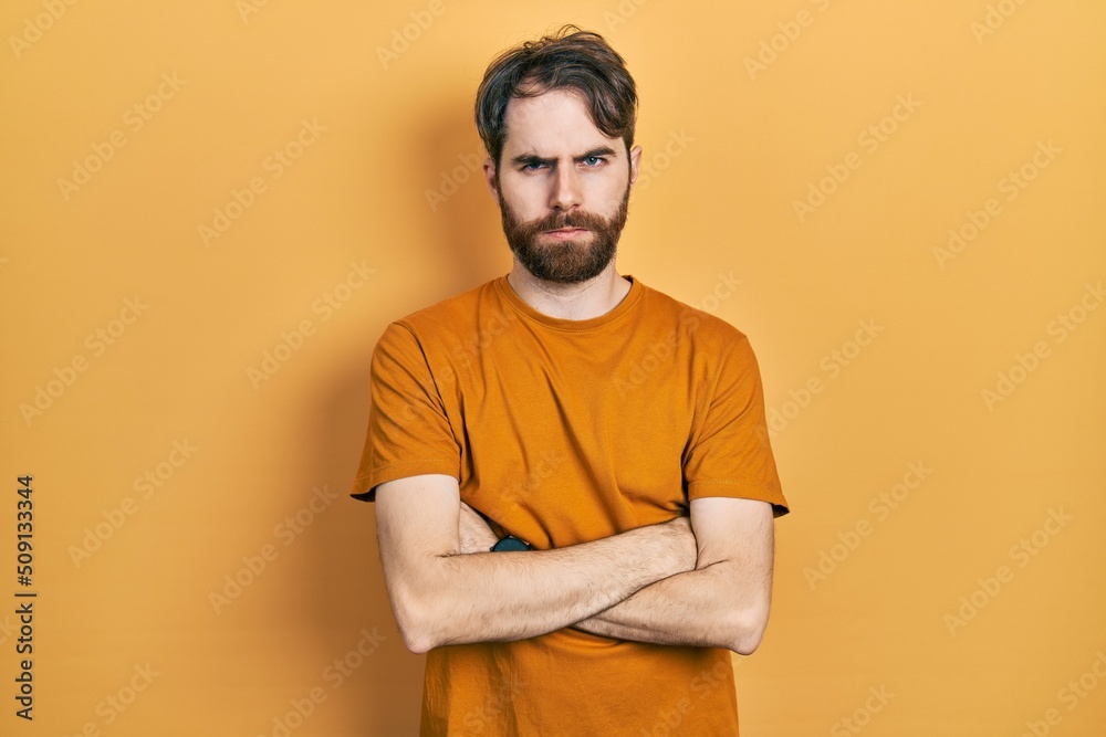 Caucasian man with beard wearing casual yellow t shirt skeptic and nervous, disapproving expression on face with crossed arms. negative person. Caucasian man with beard wearing casual yellow t shirt skeptic and nervous, disapproving expression on face with crossed arms. negative person.