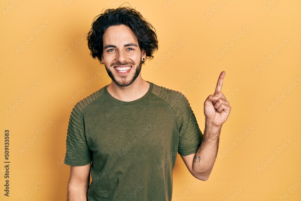 Handsome hispanic man wearing casual green t shirt smiling with an idea or question pointing finger up with happy face, number one Handsome hispanic man wearing casual green t shirt smiling with an idea or question pointing finger up with happy face, number one