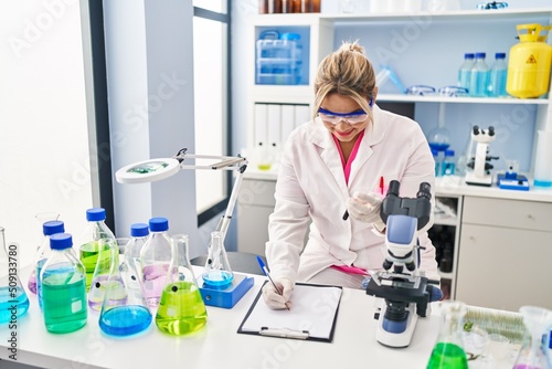 Young hispanic woman wearing scientist uniform analysing blood at laboratory