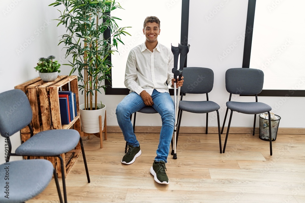 Young hispanic man waiting wearing crutches at waiting room