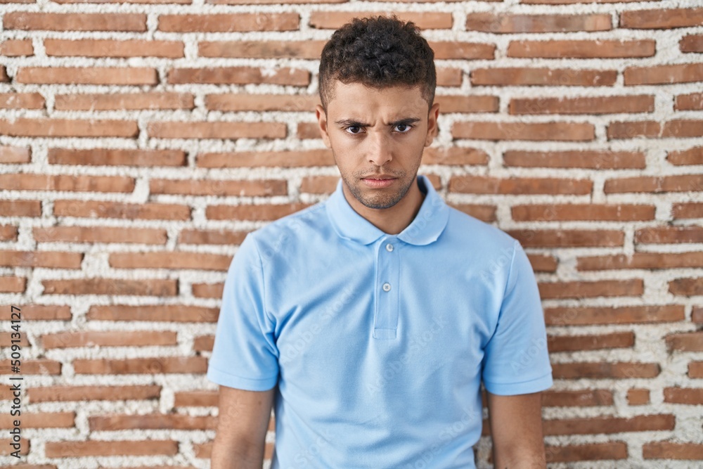 Brazilian young man standing over brick wall skeptic and nervous, frowning upset because of problem. negative person. Brazilian young man standing over brick wall skeptic and nervous, frowning upset because of problem. negative person.