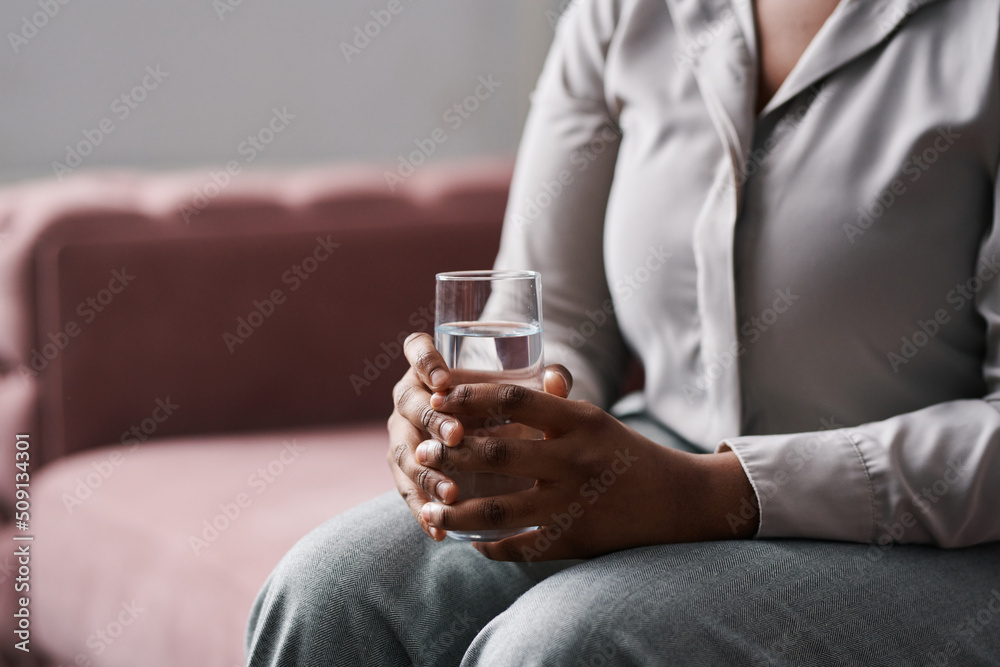 Hands of young worried female patient of counselor holding glass of water while sitting on couch and describing her problems Hands of young worried female patient of counselor holding glass of water while sitting on couch and describing her problems