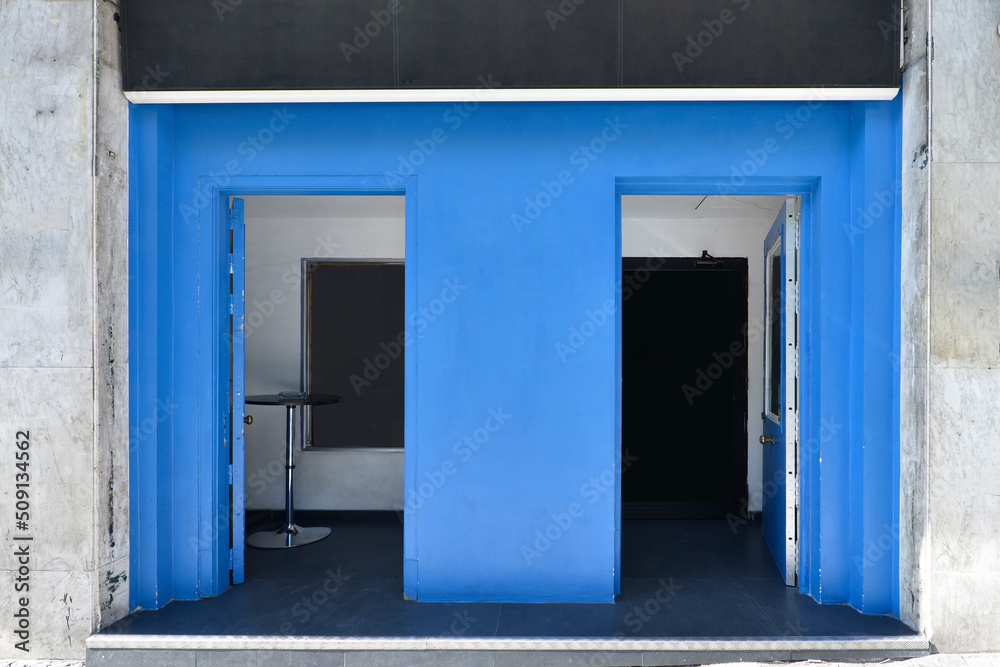 Fototapeta premium Facade of a local with walls painted in blue and black poster, table with chrome foot and black vinyl floor